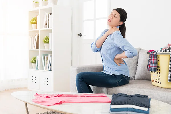 Female sitting on couch holding lower back. 