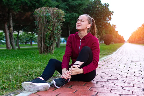 Female jogger sitting on ground holding knee in pain. 